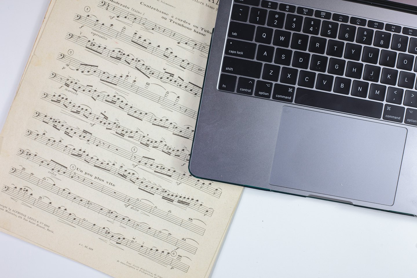 Musical notation paper next to a silver laptop on a white desk.